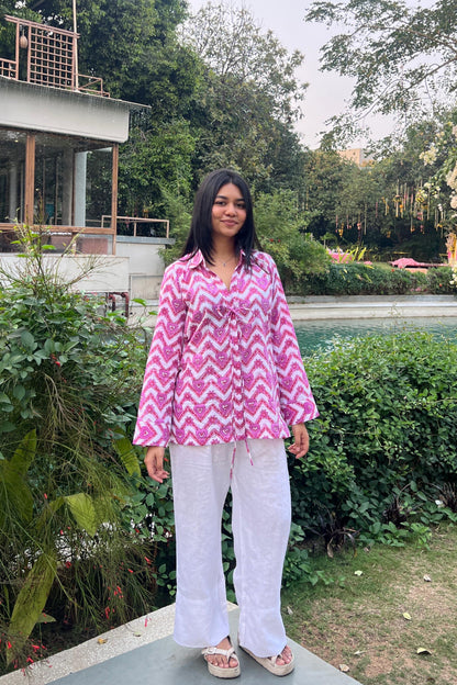 Person wearing a pink and white zigzag patterned shirt with white pants standing in a garden.