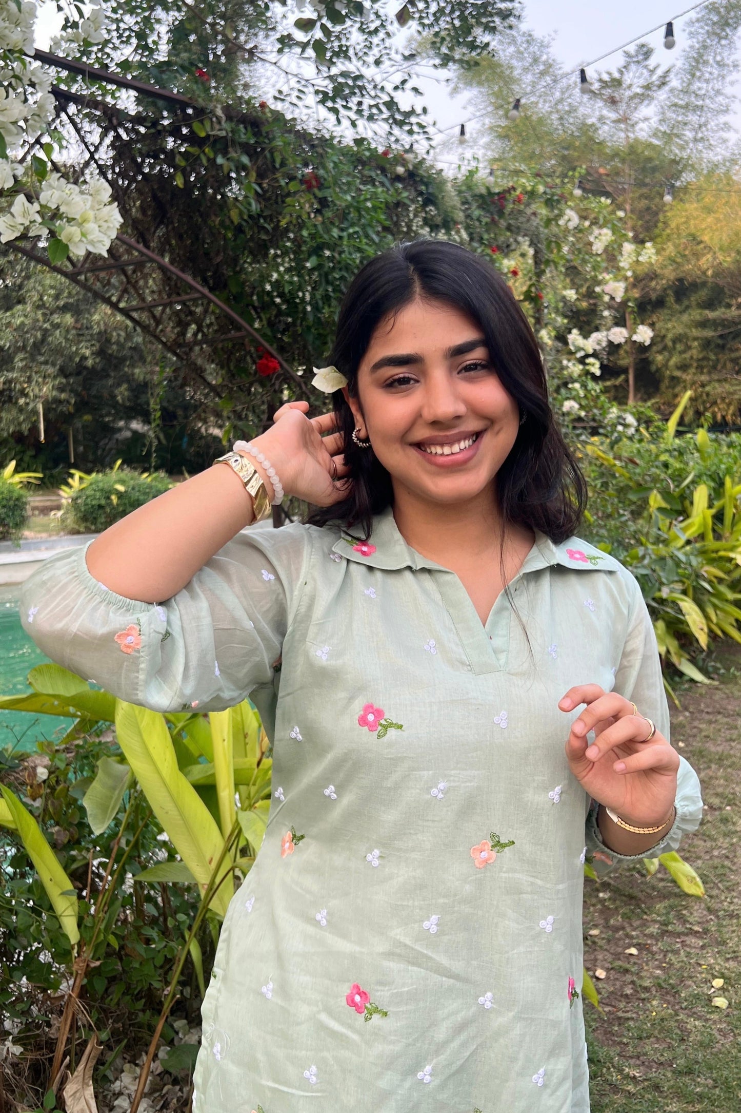 Woman in a light green traditional outfit with floral patterns standing in a garden.